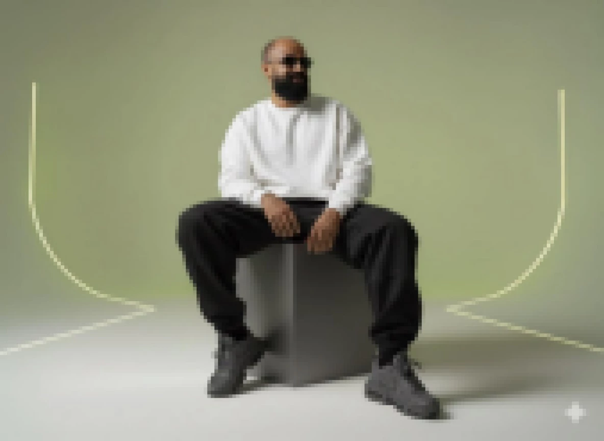 Bearded man in white sweatshirt and black joggers on cube with neon studio backdrop