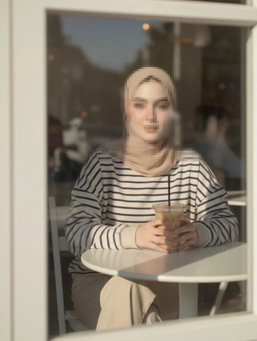 Calm woman in beige hijab enjoying iced coffee at a cozy sunlit café