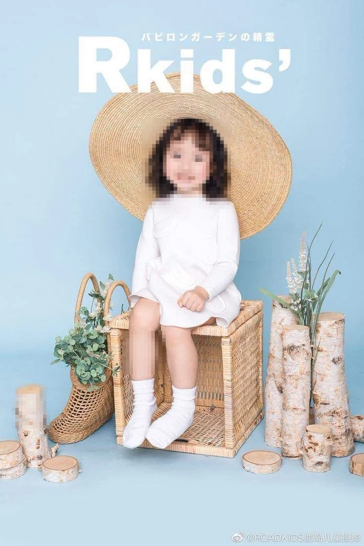 Child in white dress with straw hat on wicker cube in pastel blue studio