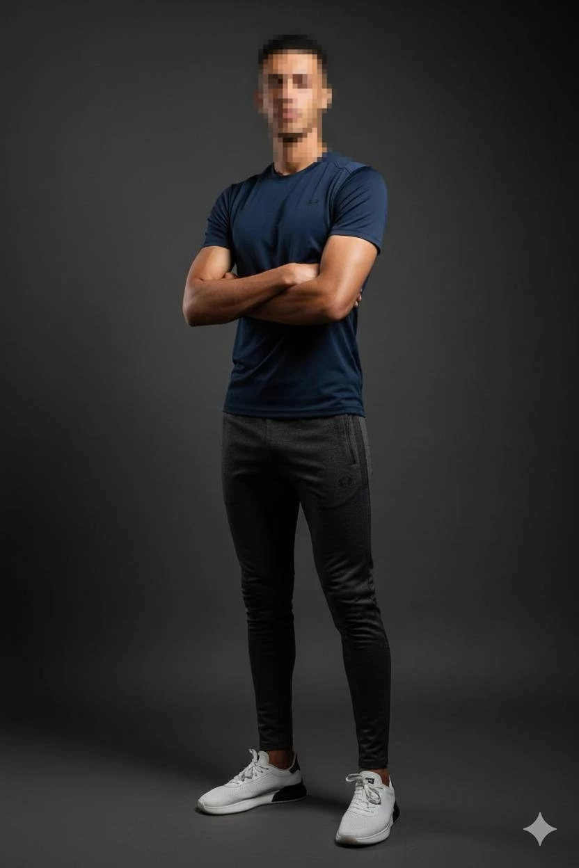 Confident man in navy t-shirt and white sneakers posing in dark studio setting