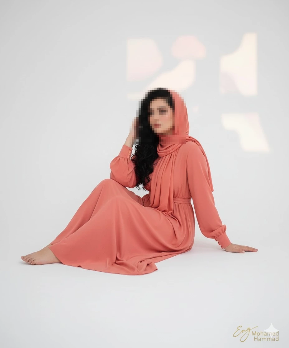Elegant woman in coral dress and headscarf sitting gracefully in minimalist studio