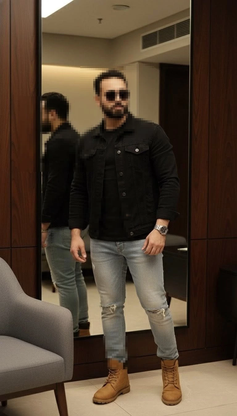 Man in black jacket and ripped jeans posing indoors with a stylish modern look