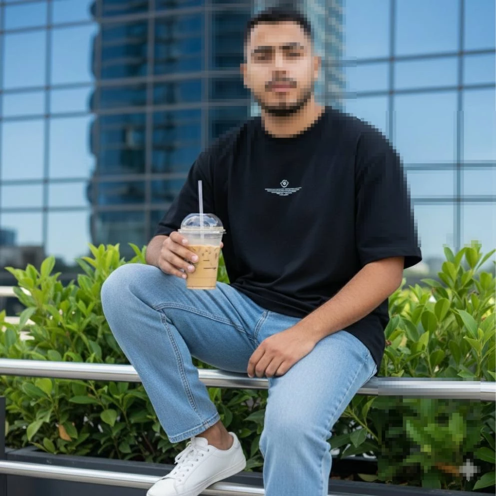 Man in Black T-Shirt and Blue Jeans Sitting Outdoors Holding Iced Coffee