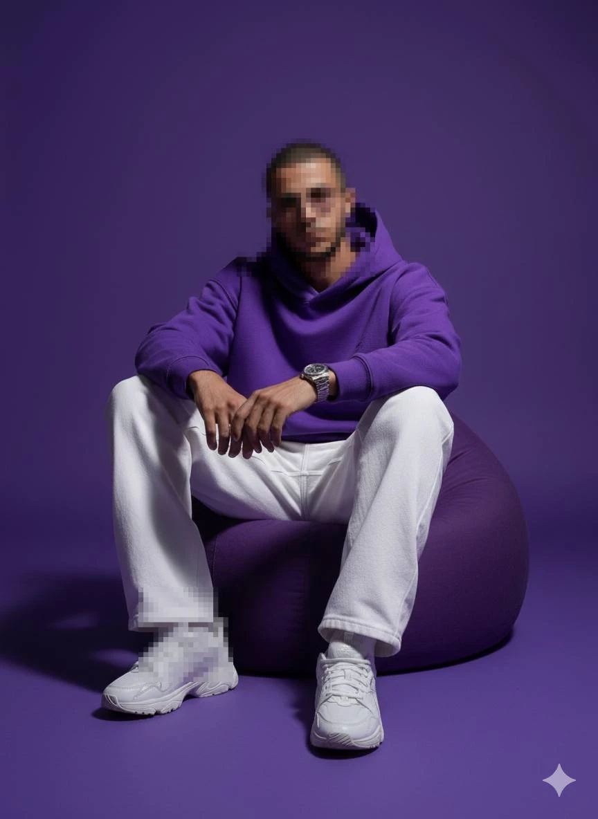 Man in Purple Hoodie and White Pants Sitting Confidently in Studio Setting