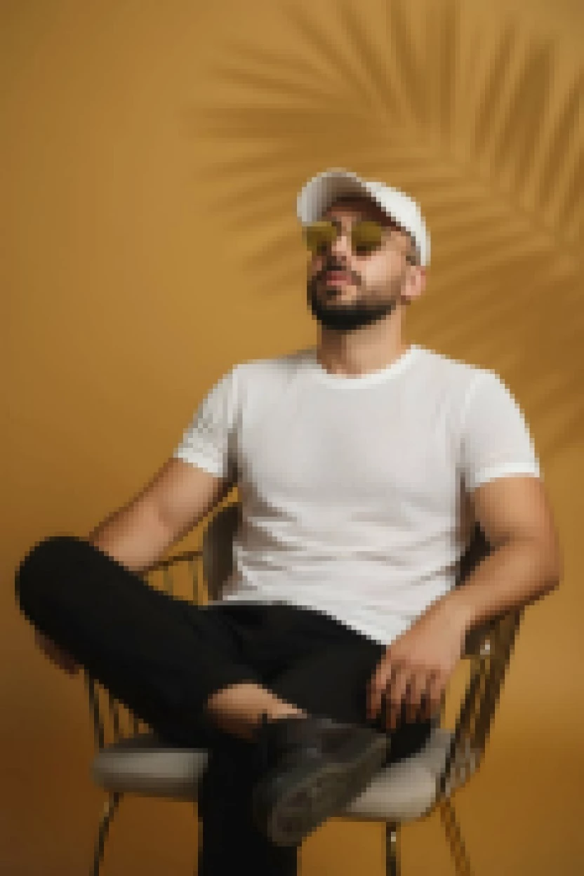 Man in white t shirt and cap sitting confidently on chair with yellow background