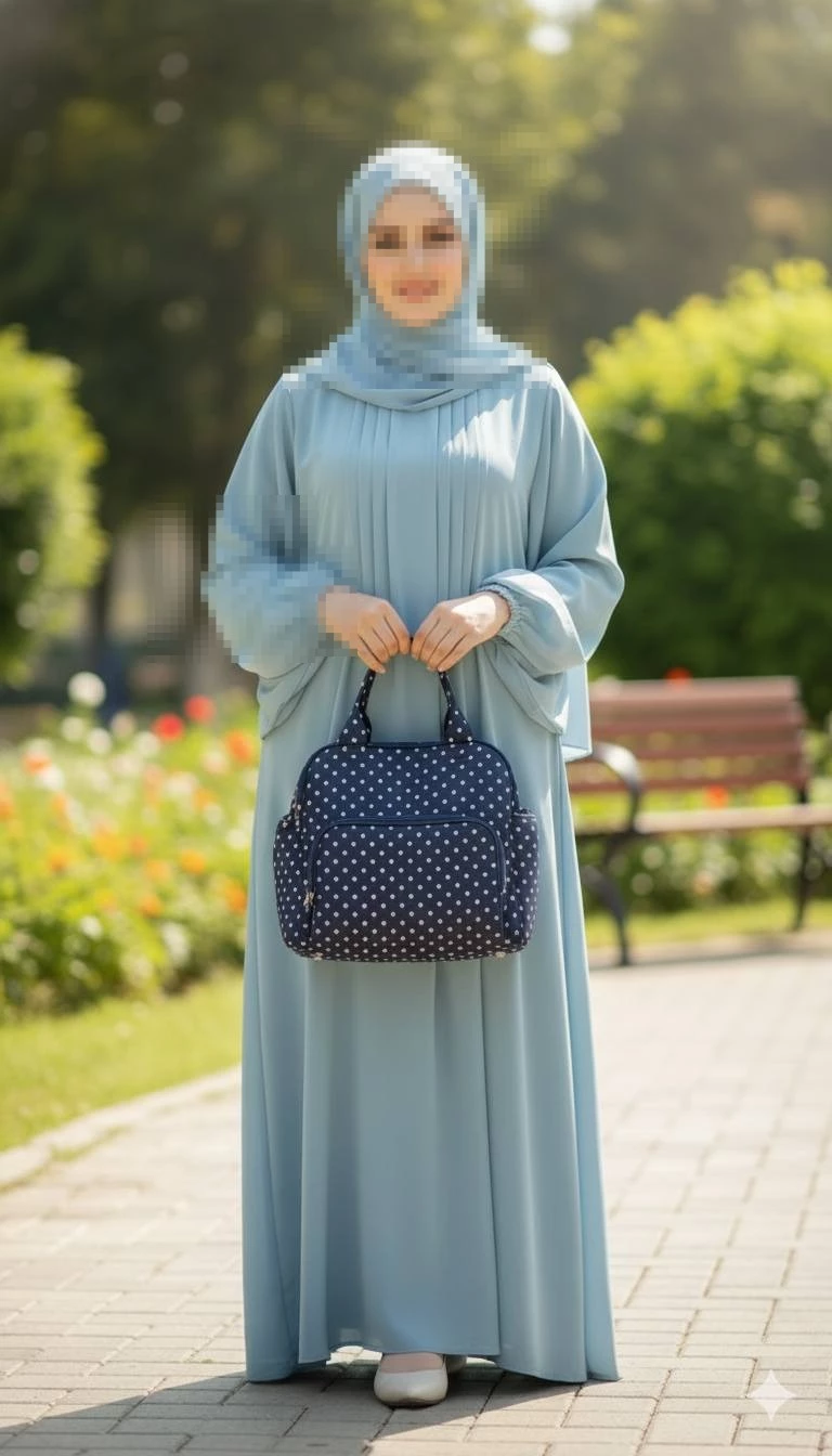 Modest outdoor portrait of a woman in a light blue abaya holding a navy polka dot bag