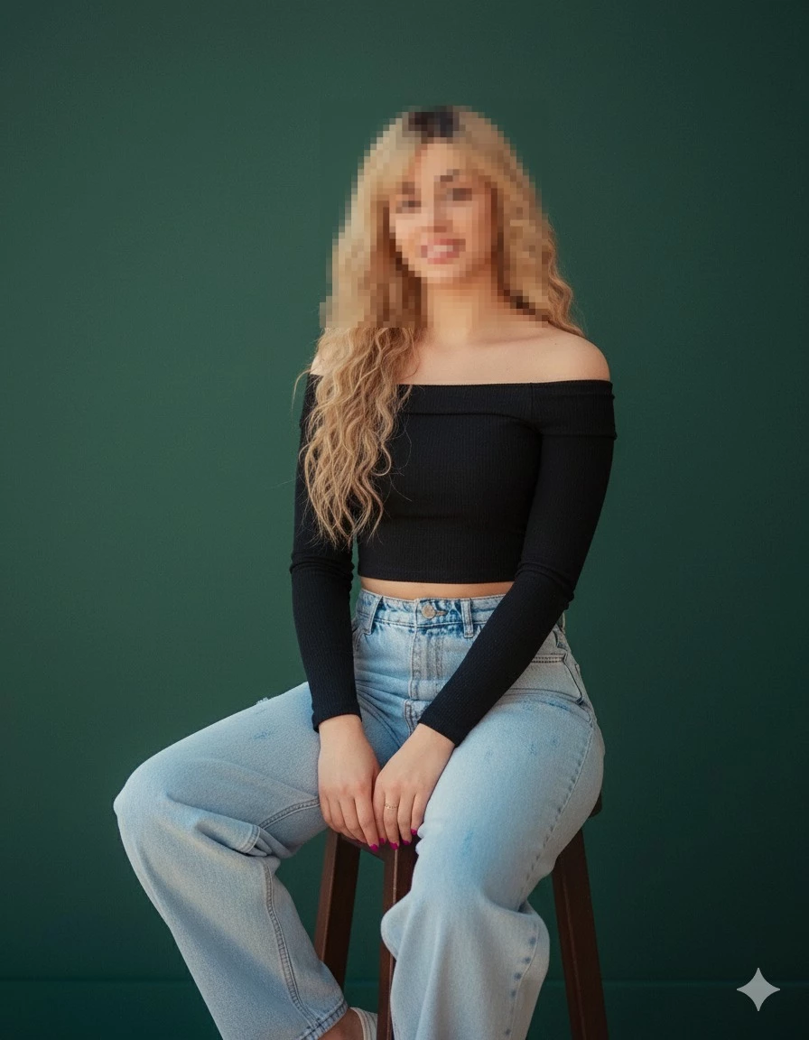 Stylish woman in black off shoulder top and light blue jeans sitting on stool