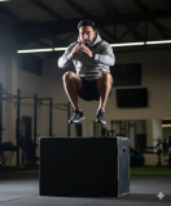 Athletic man jumping onto box wearing grey hoodie during gym workout session