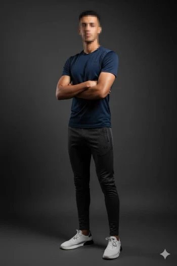 Confident man in navy t-shirt and white sneakers posing in dark studio setting