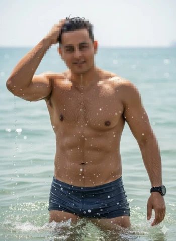 Confident man standing in the sea wearing dark blue swim shorts under sunlight