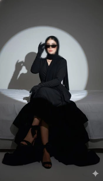 Elegant woman in all-black outfit sitting under spotlight with confident pose