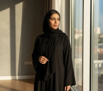 Elegant Woman in Black Abaya Standing by Window in Warm Sunlight