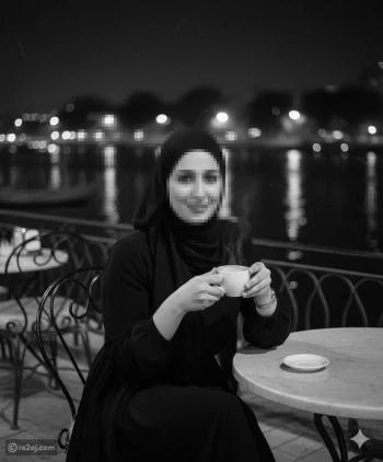 Elegant woman in black hijab enjoying coffee at riverside café at night