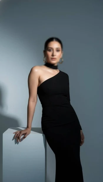 Elegant woman in black one-shoulder dress posing confidently in modern studio