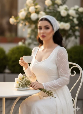 Elegant woman in white dress enjoying tea at outdoor café surrounded by roses
