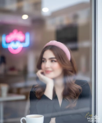 Elegant woman with pink headband enjoying coffee by a café window
