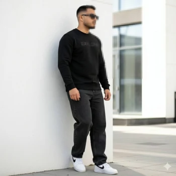 Man in black Explore sweatshirt leaning on white wall in modern city setting