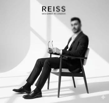 Man in black suit sitting on chair holding glasses in minimalist studio