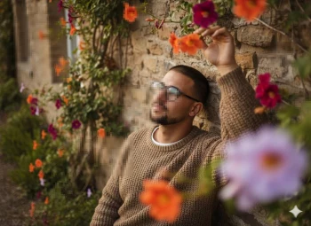Man in brown sweater relaxing by stone wall surrounded by colorful blooming flowers