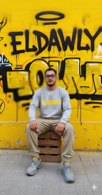 Man in casual streetwear posing in front of yellow graffiti wall with Eldawly text