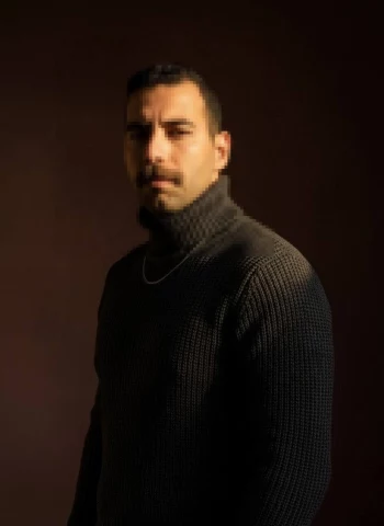 Man in dark turtleneck sweater posing under warm cinematic lighting