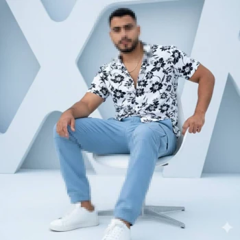 Man in floral shirt and blue pants sitting on a white chair in modern studio