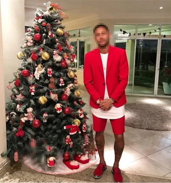 Man in Red Outfit Posing Beside a Decorated Christmas Tree Indoors