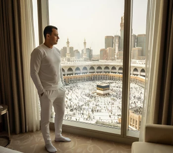 Man in white outfit admiring Kaaba view from hotel window in Mecca