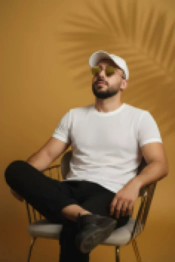 Man in white t shirt and cap sitting confidently on chair with yellow background
