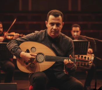 Man playing oud on stage with live orchestra during traditional music concert