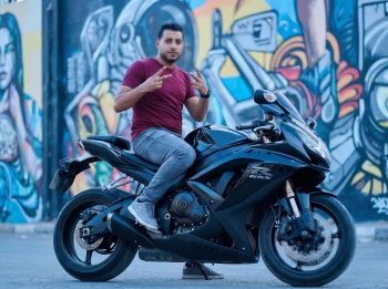 Man Posing on a Black Suzuki GSX Motorcycle in Front of Colorful Graffiti Art