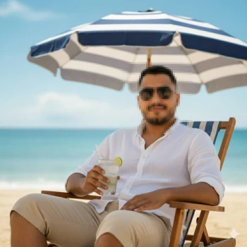 Man relaxing on the beach with a drink under a blue and white umbrella