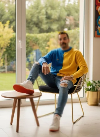 Man sitting indoors wearing blue and yellow sweater with casual modern style