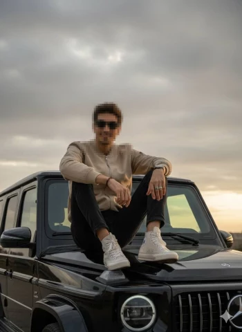 Man sitting on black Mercedes G-Class at sunset wearing beige jacket and sneakers