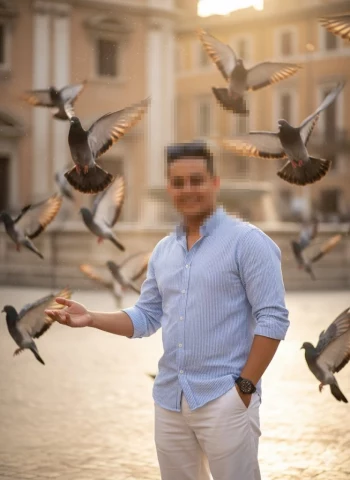 Man smiling in sunny square surrounded by flying pigeons at golden hour