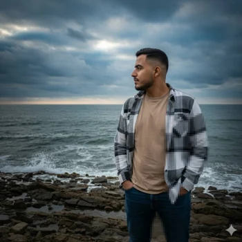 Man standing on rocky seashore wearing beige shirt and checkered jacket