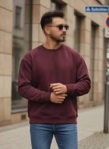 Man wearing burgundy sweatshirt and blue jeans standing confidently on city street