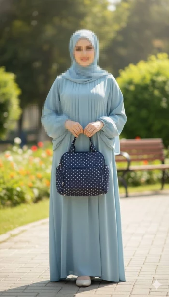 Modest outdoor portrait of a woman in a light blue abaya holding a navy polka dot bag