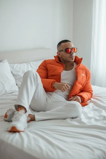Relaxed man in orange jacket posing on a white bed in a bright modern room