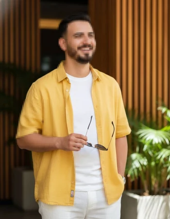 Smiling man in yellow shirt holding sunglasses outdoors in sunny modern setting