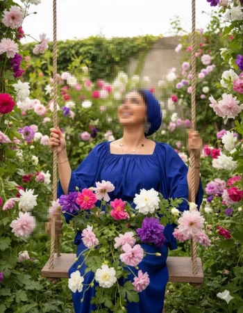 Smiling woman in blue dress on swing surrounded by colorful blooming flowers