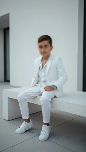 Stylish Boy in All White Suit Sitting on Modern Bench Outdoors