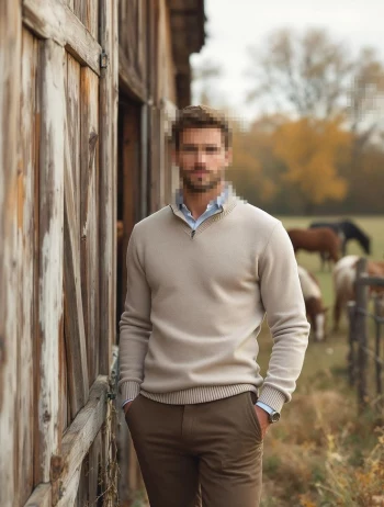 Stylish Man in Beige Sweater Posing Outdoors Near Wooden Stable and Horses