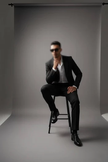 Stylish Man in Black Suit and Sunglasses Sitting Confidently in Studio