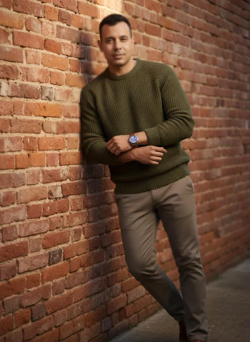 Stylish Man in Olive Green Sweater Leaning Against Brick Wall Outdoors