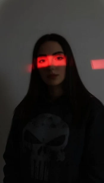 Woman in dark hoodie illuminated by red light beam across her eyes