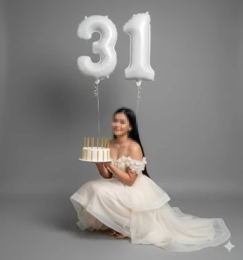Woman in elegant cream dress holding birthday cake with number 31 balloons