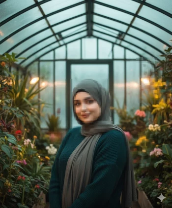 Woman in grey hijab standing in greenhouse surrounded by vibrant green plants