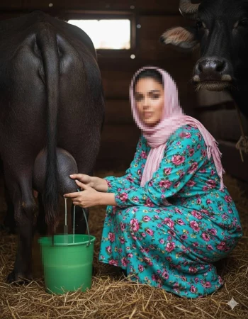 Woman milking a buffalo in a rustic barn wearing floral turquoise dress and scarf