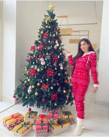 Woman Posing Beside a Decorated Christmas Tree with Gifts in a Cozy Holiday Setting